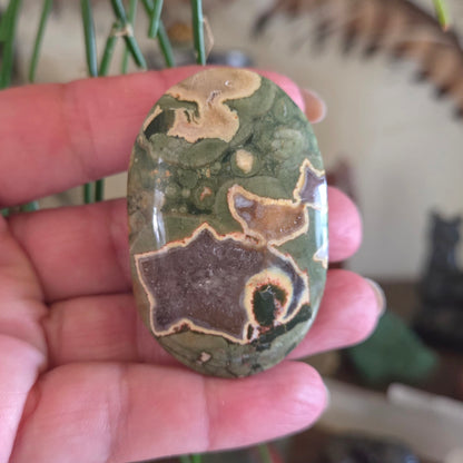 Hand holding a green and brown patterned stone with blurred background