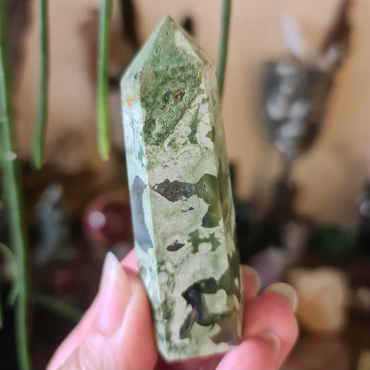 A hand holding a Rhyolite Point, with a green and white color pattern.