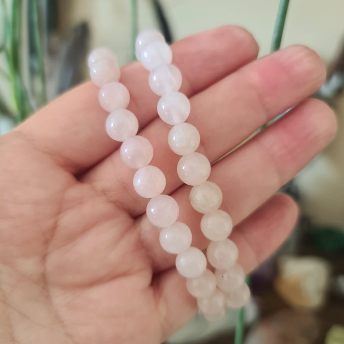 A hand holding a rose quartz bracelet with round beads.