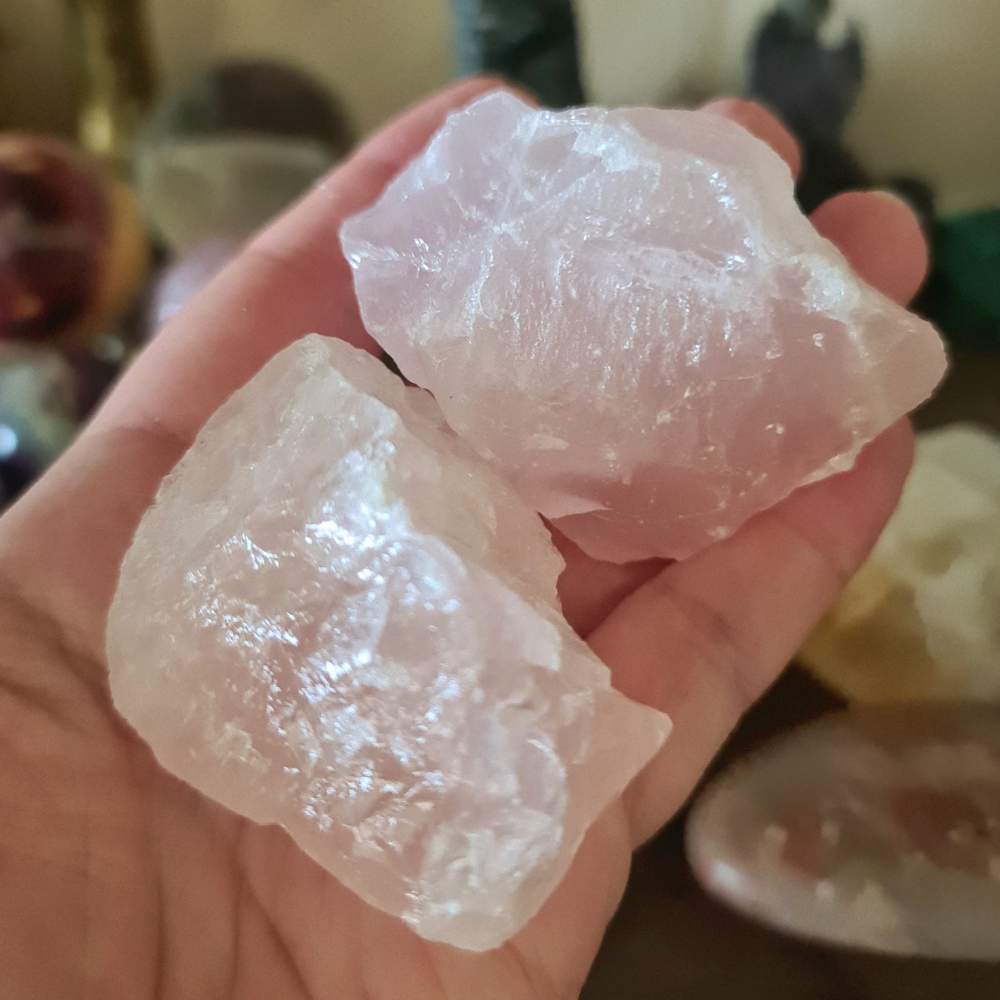 Two polished rose quartz crystal chunks held in a person's hand, with a blurred background suggesting a focus on the stones.