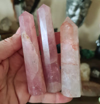 A hand holding a polished pink rose quartz crystal point, with a few drops of water visible on the surface.