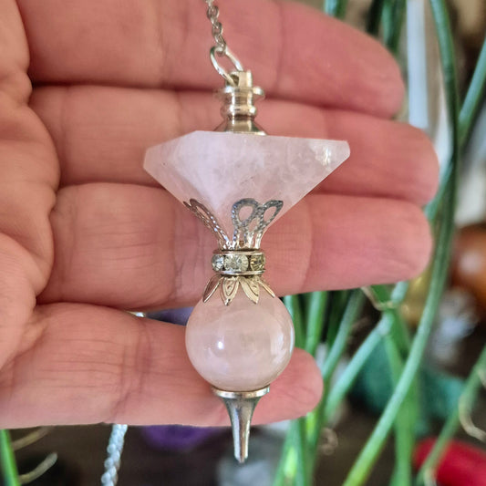A hand holding a rose quartz pendulum with silver-colored metal accents.