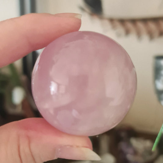 A person holding a pink rose quartz sphere with a smooth surface.