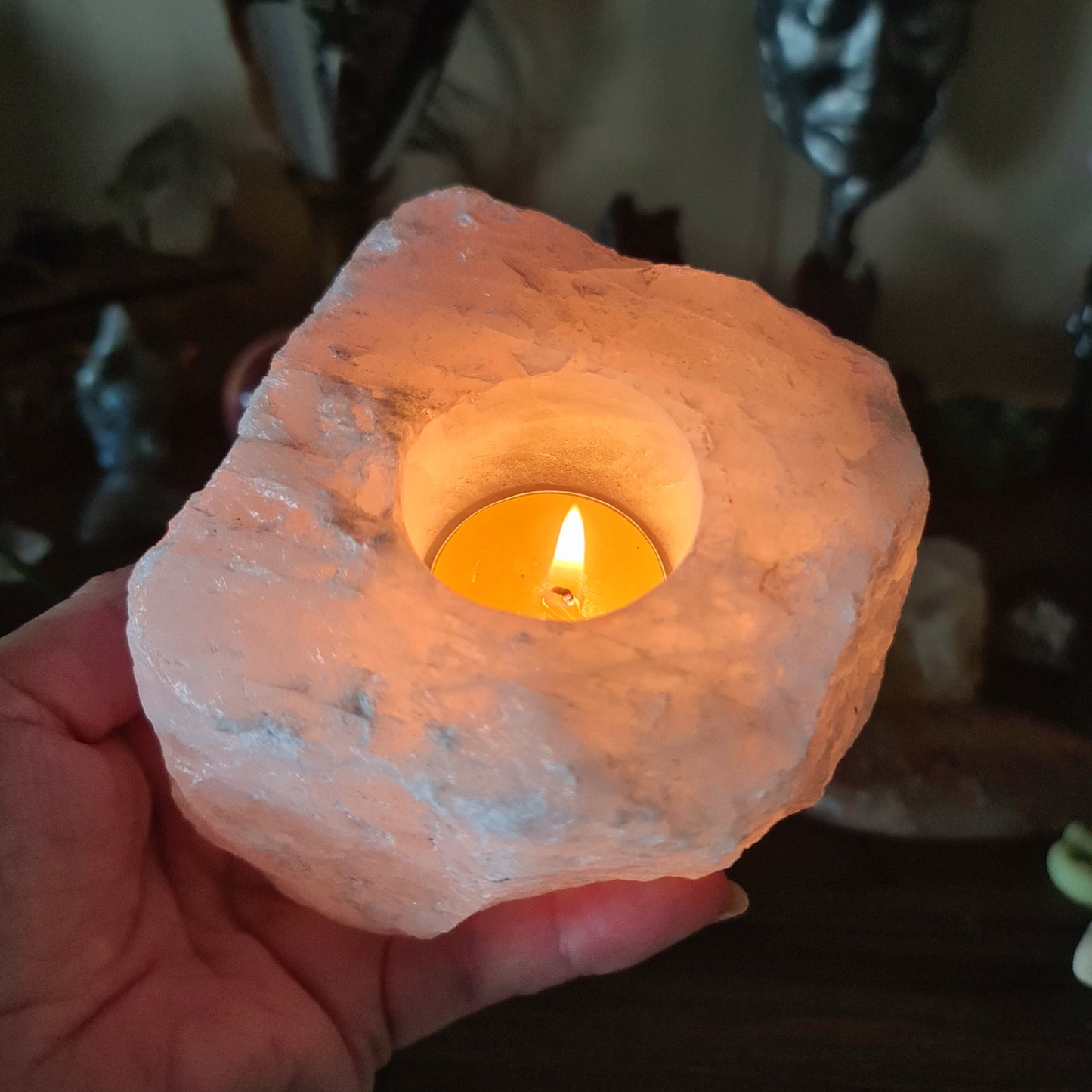 A person holding a Rose Quartz tealight holder with a lit candle inside, showcasing the pink crystal's interior.