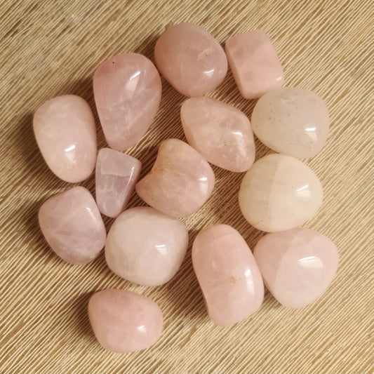 A collection of polished rose quartz stones with a light pink color, displayed on a wooden surface.