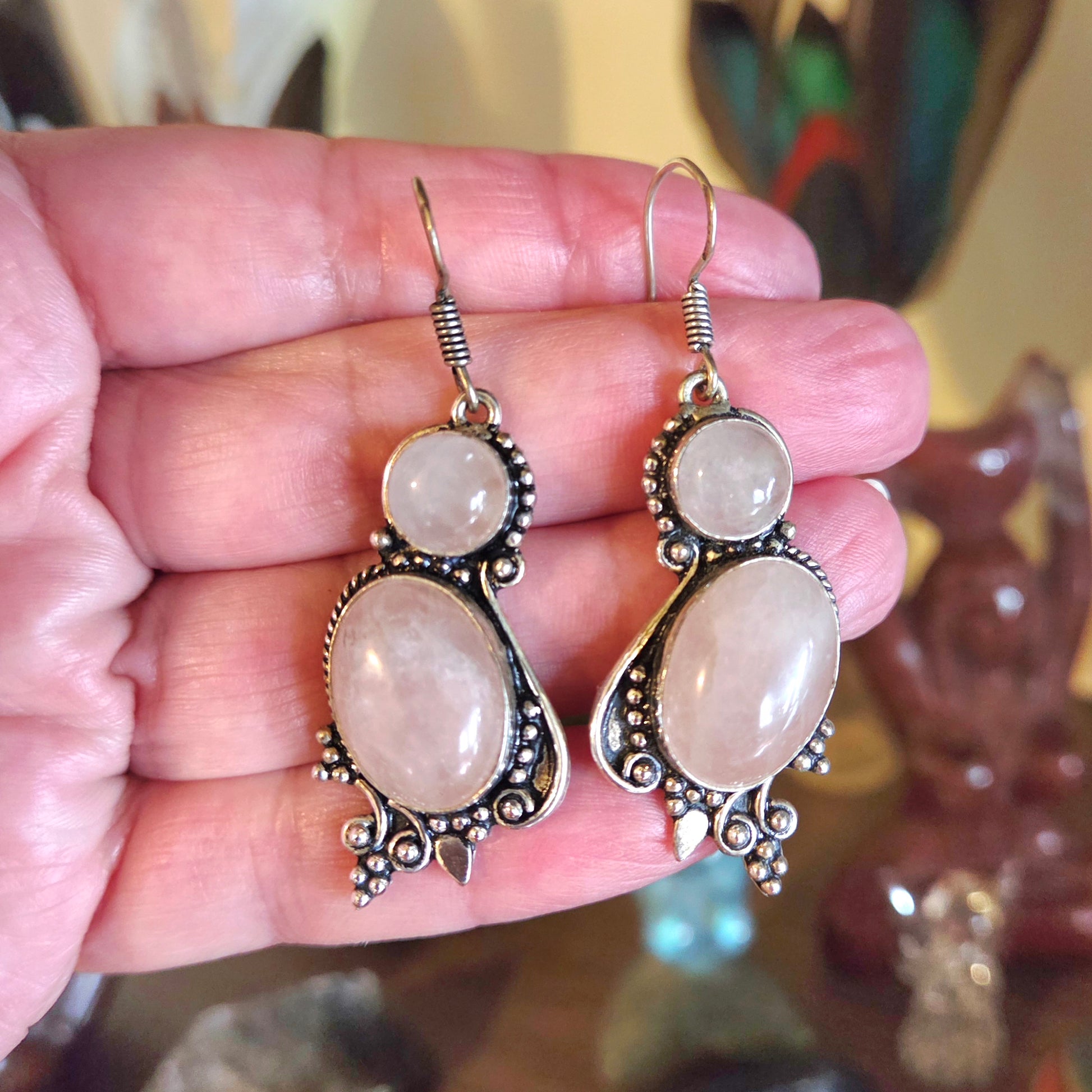 Pair of silver earrings with large beige stones held in a hand against a blurred background.