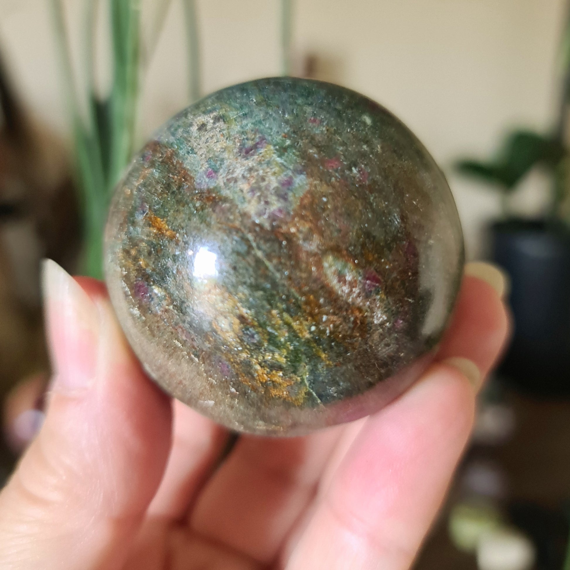 A hand holding a polished Ruby Fuchsite sphere with a marbled green appearance.