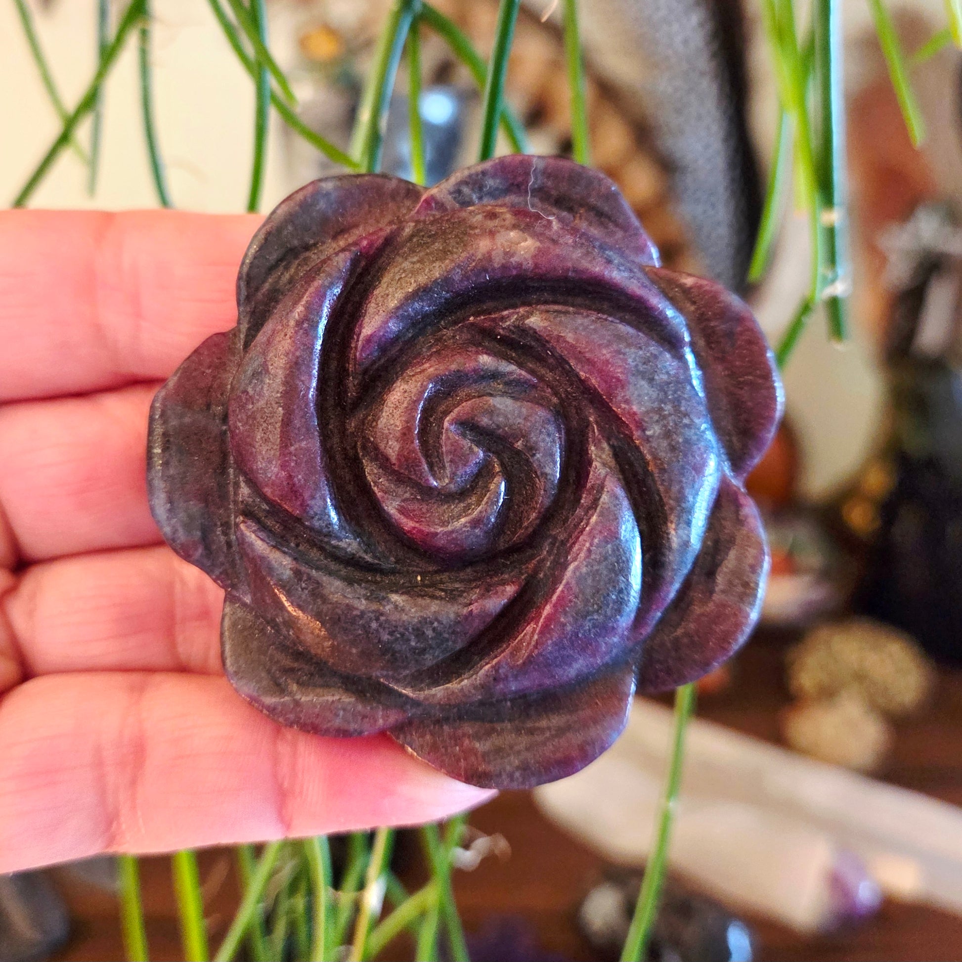 A hand holding a rough, unpolished gemstone shaped like a rose with swirls of purple and black colors.