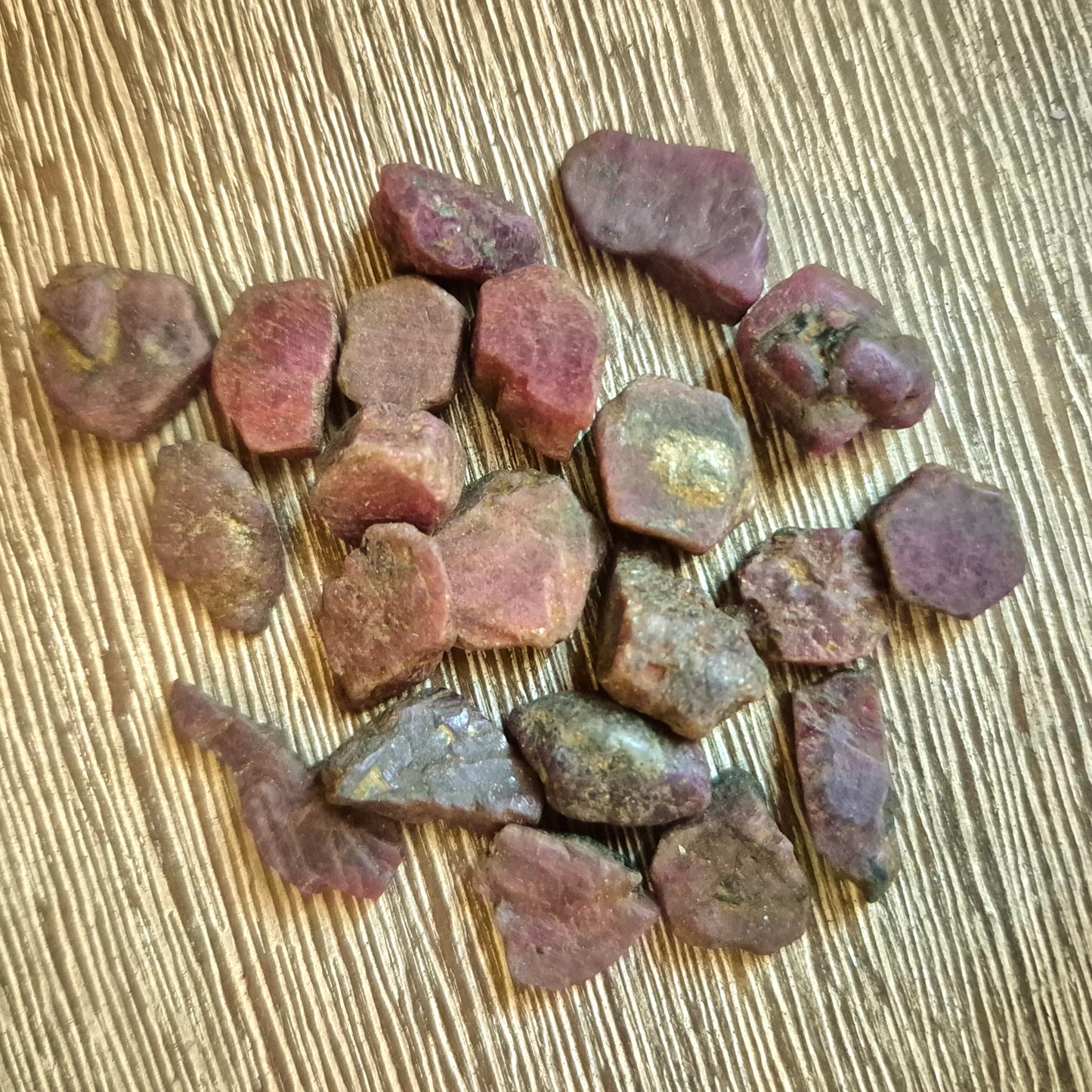 A collection of small, irregularly shaped ruby tumble stones displayed on a textured surface.