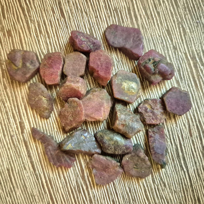 A collection of small, irregularly shaped ruby tumble stones displayed on a textured surface.