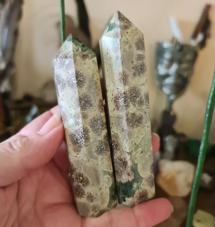 A hand holding a polished piece of Russian Flower Agate with a greenish hue and patterns resembling a flower.