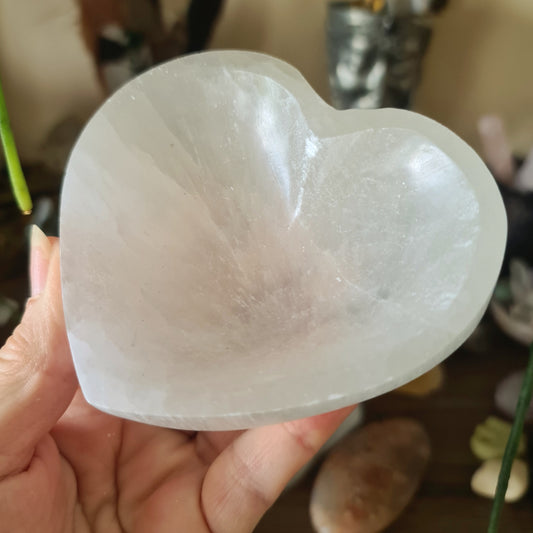 A heart-shaped selenite crystal bowl being held by a person.