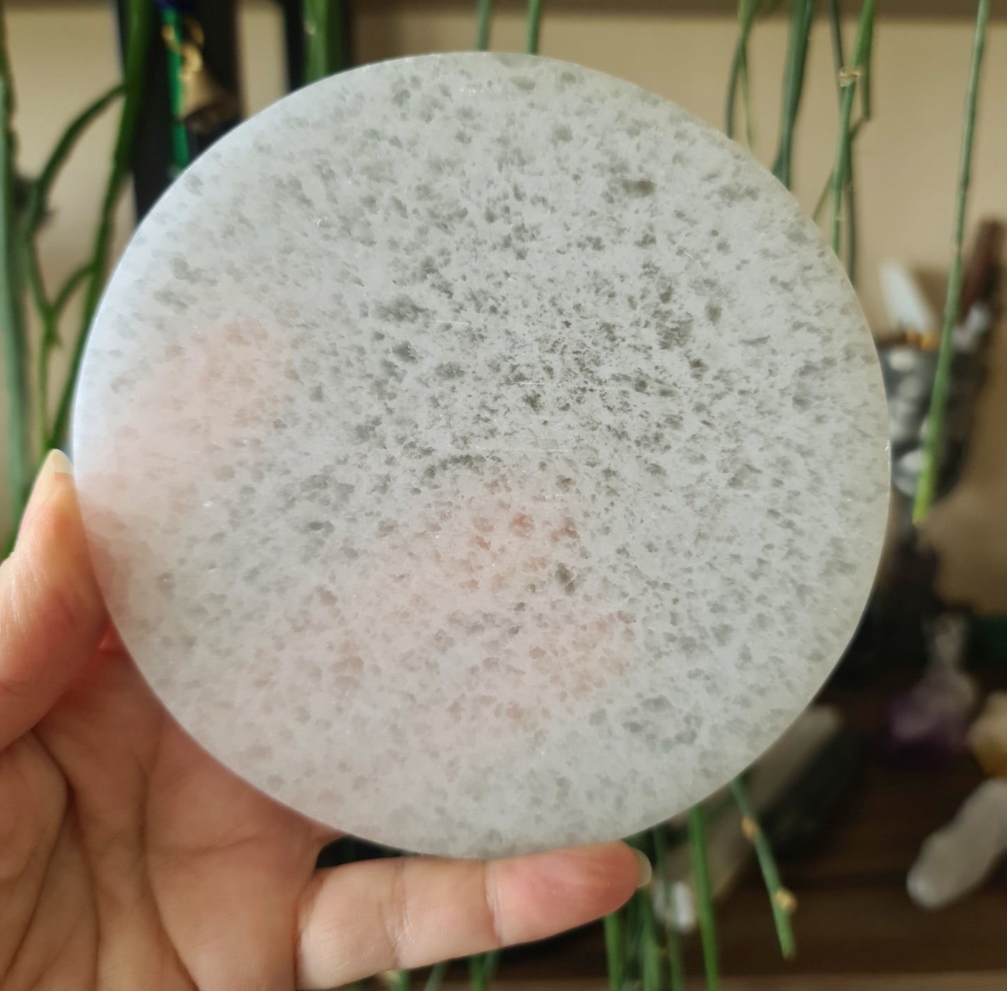 A hand holding a large, round, white selenite charging plate.