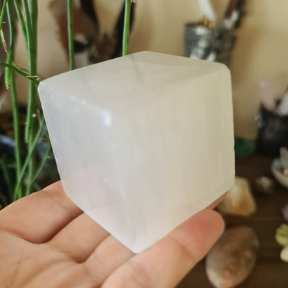 A person holding a small white selenite crystal cube.
