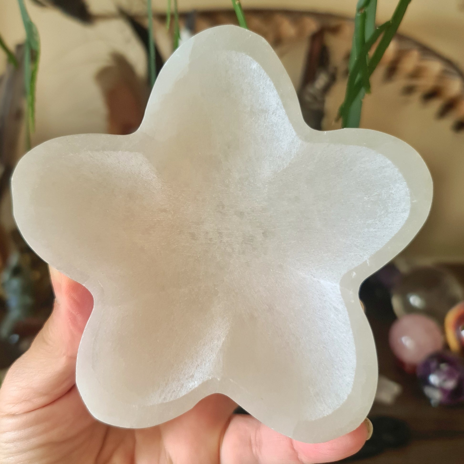 A white selenite flower-shaped decorative bowl held in a person's hand.