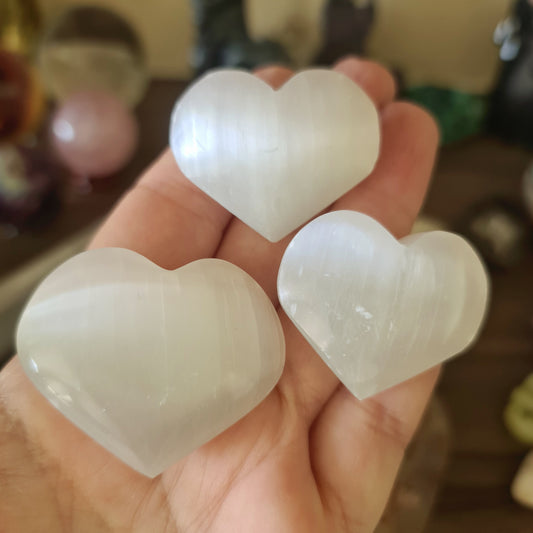 Three heart-shaped selenite stones held in a person's hand.
