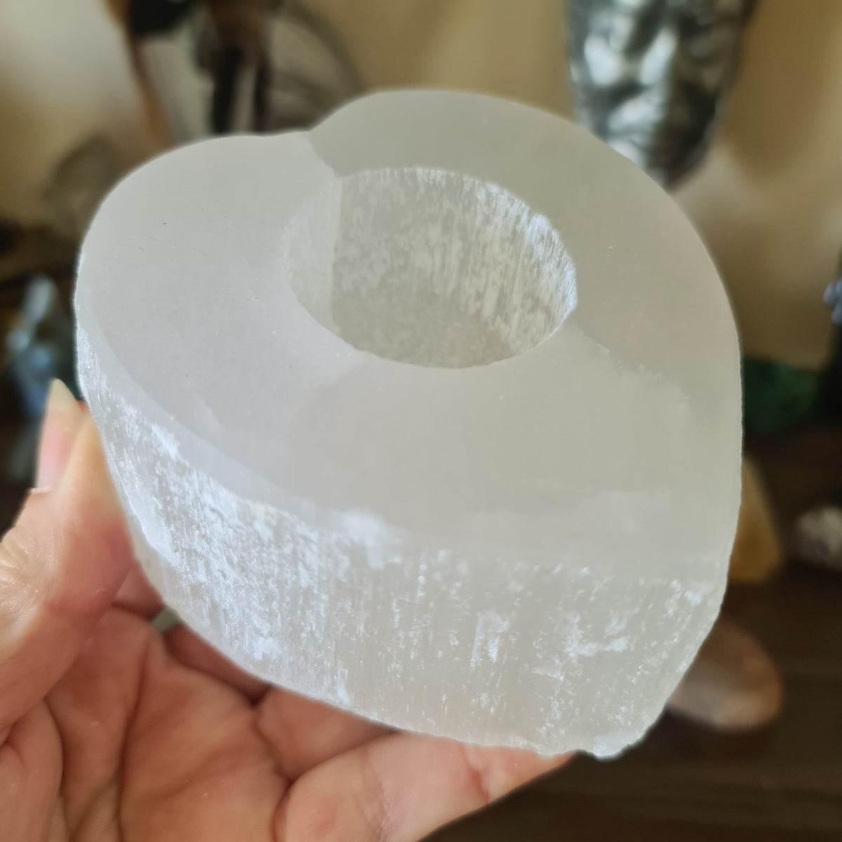A clear selenite crystal tealight holder being held by a hand.