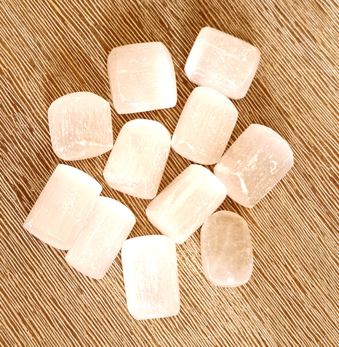 A collection of polished selenite tumbles on a wooden surface.
