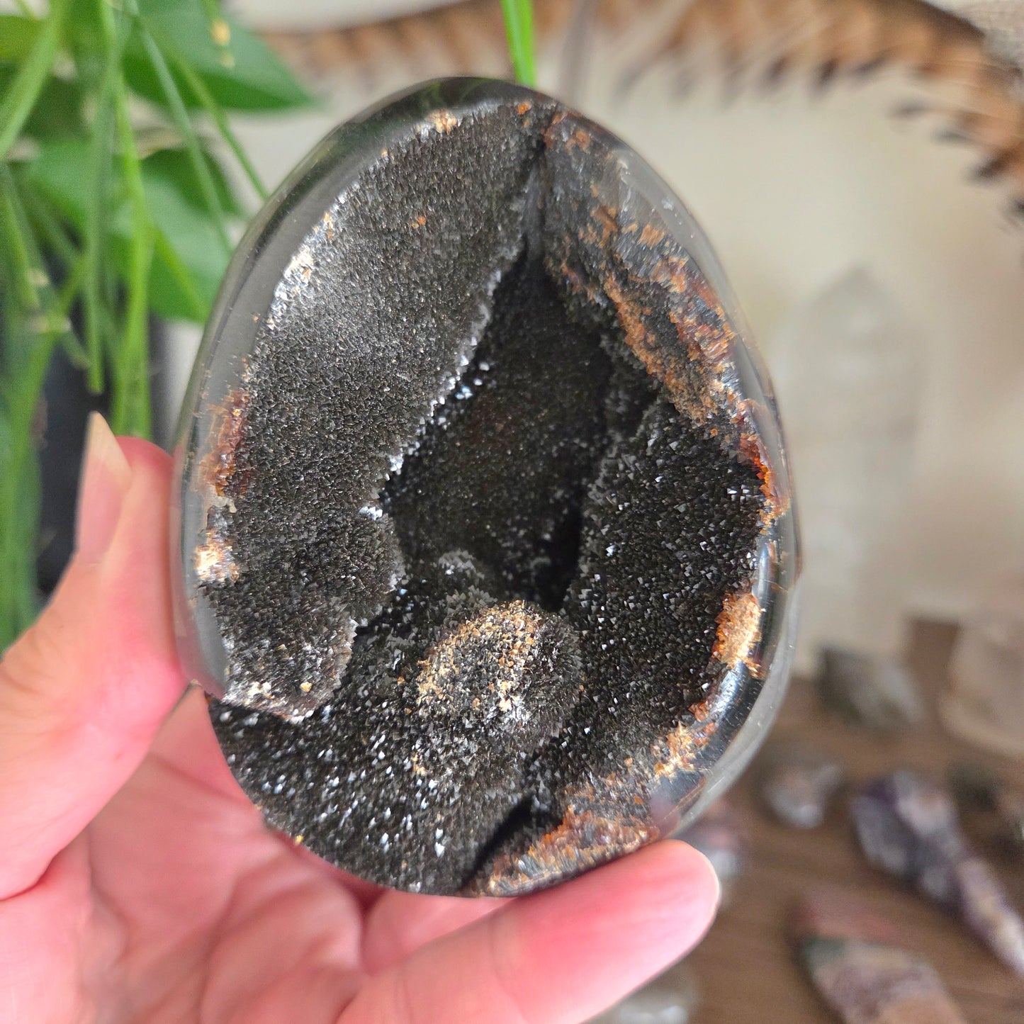 Close-up of a hand holding a black geode crystal with a blurred background