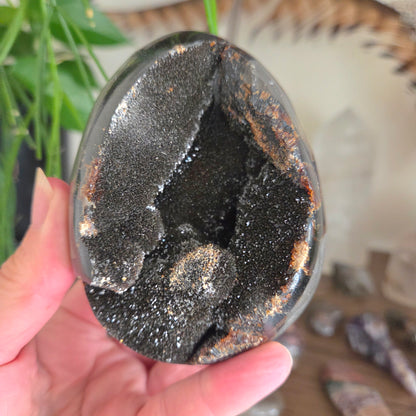 Close-up of a hand holding a black geode crystal with a blurred background
