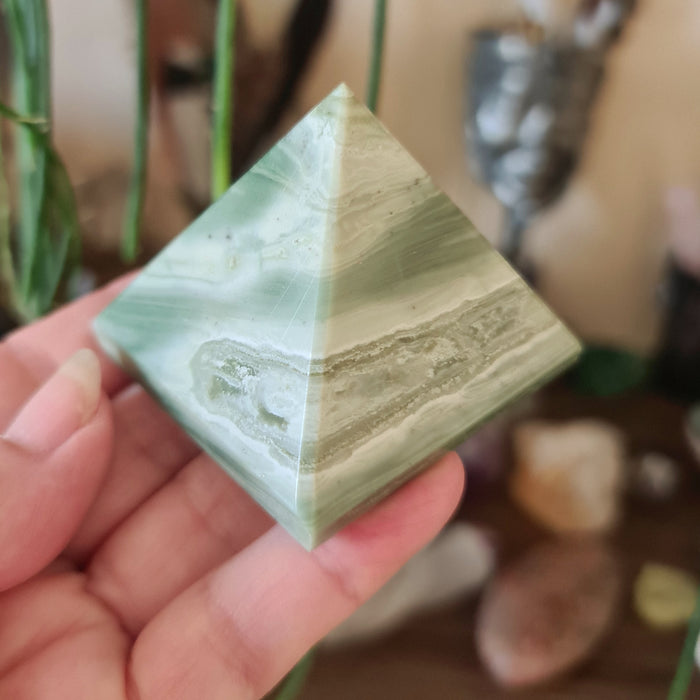 A green serpentine stone pyramid held in a person's hand, with a blurred background suggesting a focus on the stone.