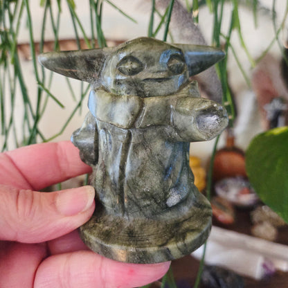 A hand holding a carved stone figurine of Yoda from Star Wars.