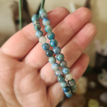 A hand holding a multicolored beaded bracelet with a mix of blue, green, and brown colors.