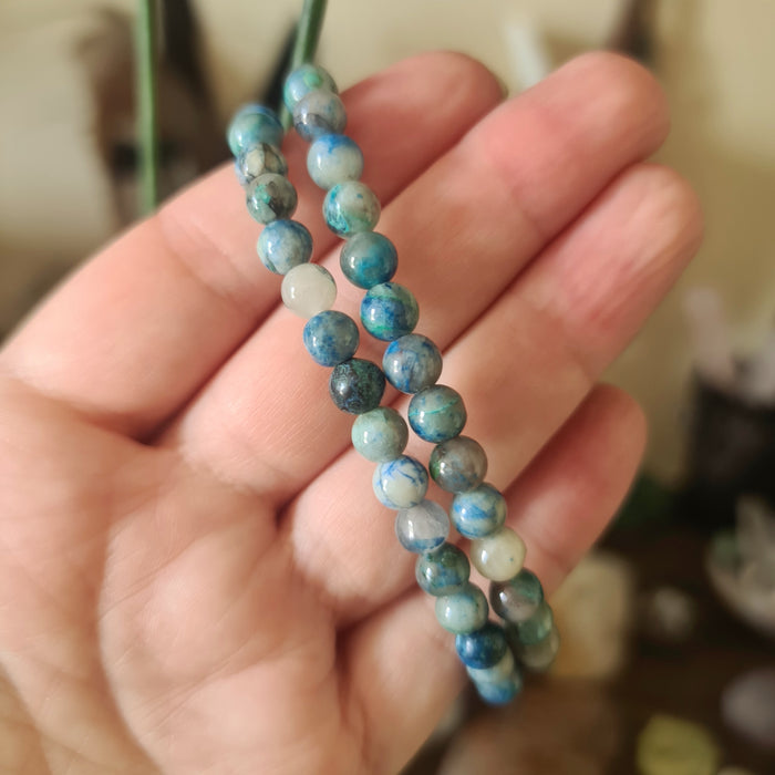 A hand holding a multicolored beaded bracelet with a mix of blue, green, and brown colors.