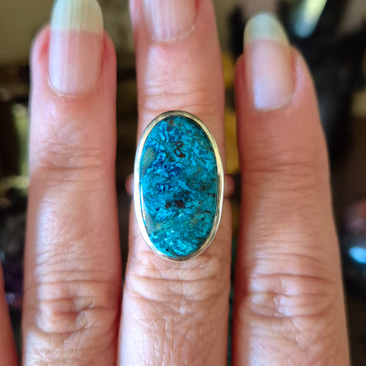 A hand holding a Shattuckite ring with blue and green marbling, mounted on a gold band.