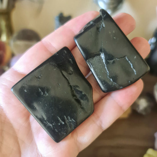 Two black shungite tiles being held in a person's hand.