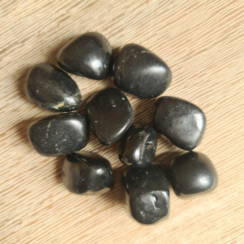 A collection of black shungite tumble stones on a wooden surface.