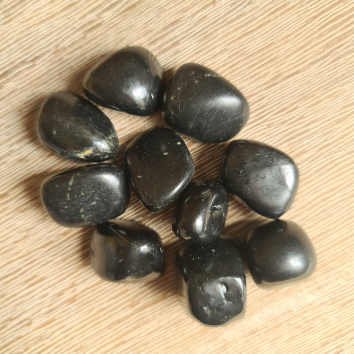 A collection of black shungite tumble stones on a wooden surface.