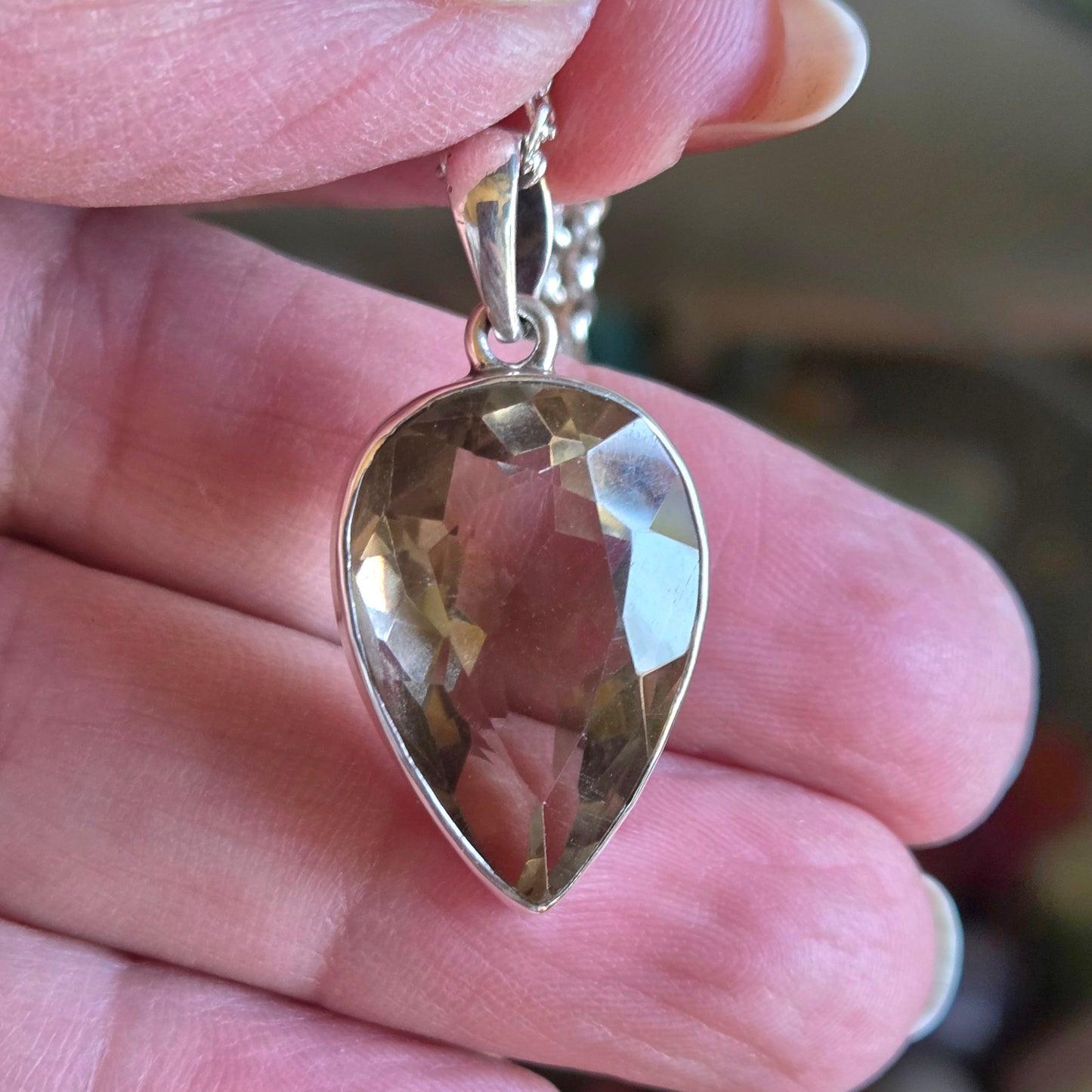 Gold teardrop pendant held between fingers with a blurred background