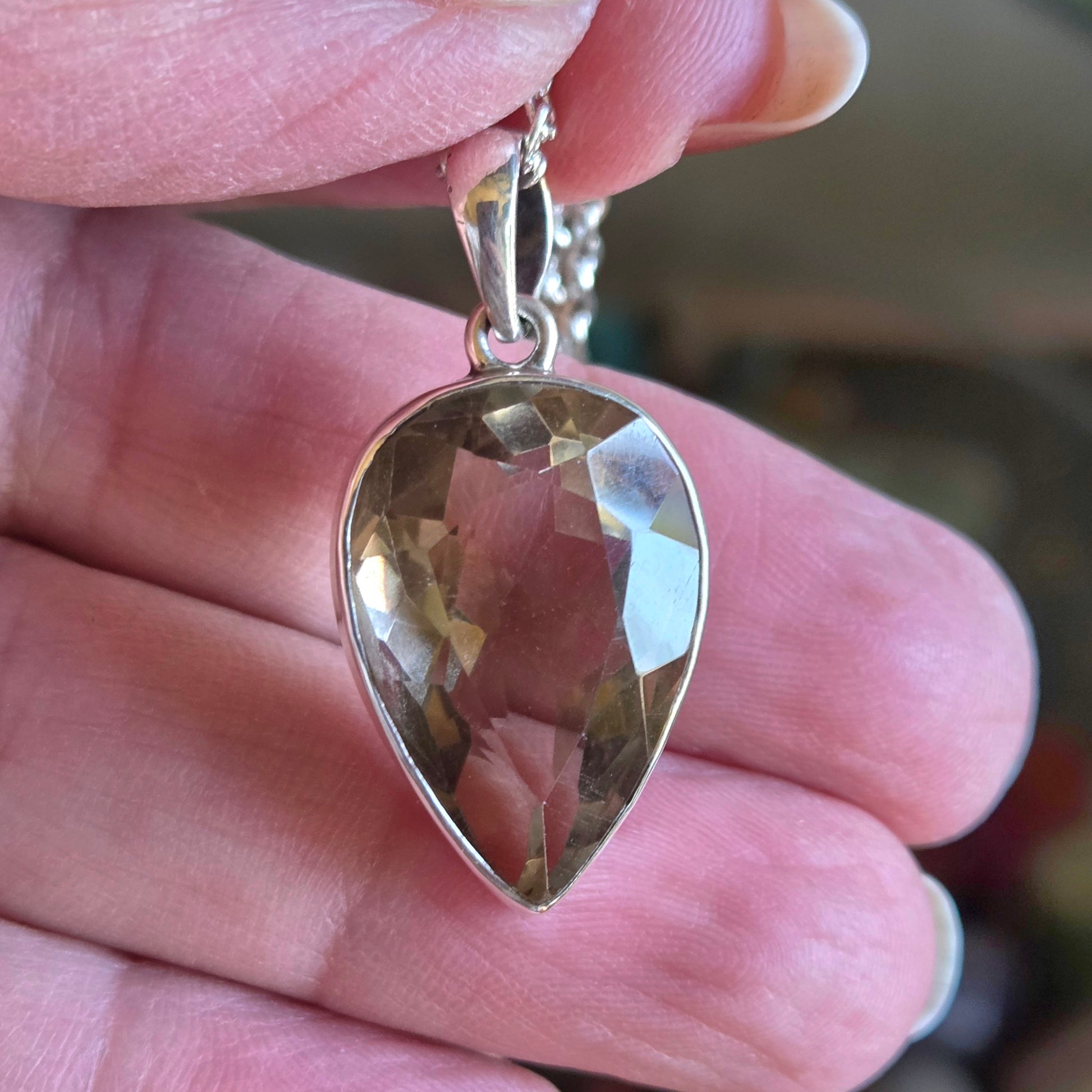 Gold teardrop pendant held between fingers with a blurred background