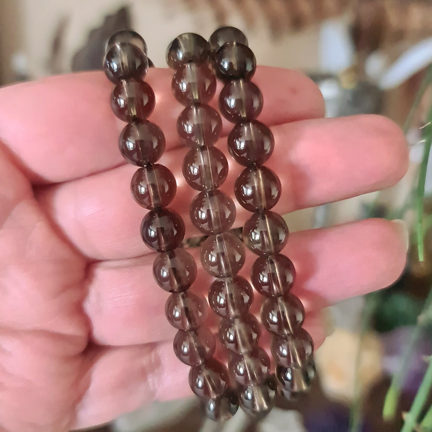A hand holding a smoky quartz beaded bracelet with a dark-black to brownish-grey color range.