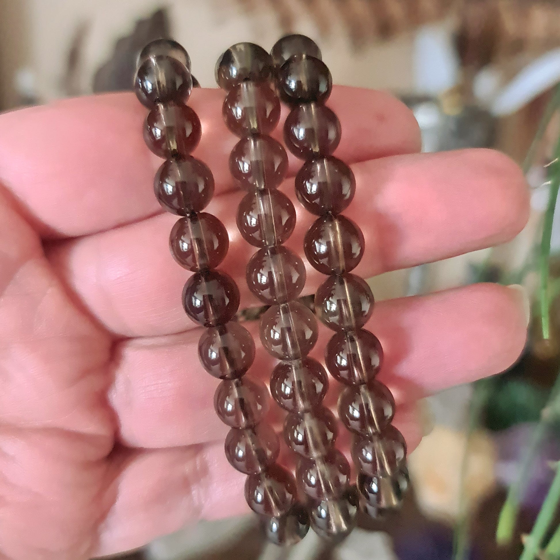 A hand holding a smoky quartz beaded bracelet with a dark-black to brownish-grey color range.