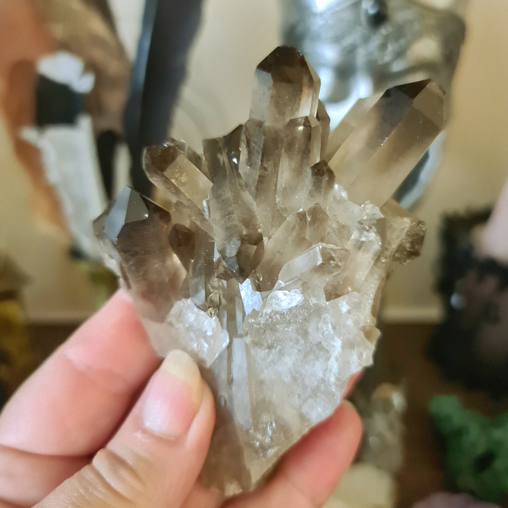 A hand holding a smoky quartz crystal cluster with a translucent brownish-grey color.