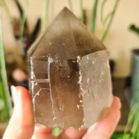 A smoky quartz crystal with a cut base point, held in a person's hand.