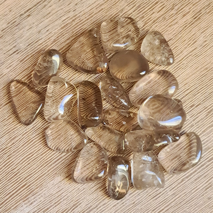 A collection of smoky quartz tumbles with a translucent brown color, displayed on a wooden surface.