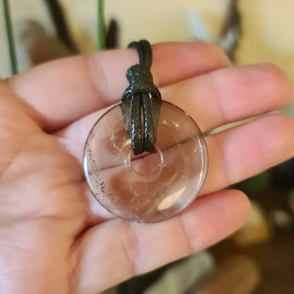A smoky quartz donut pendant held in a person's hand, with a black leather cord attached.
