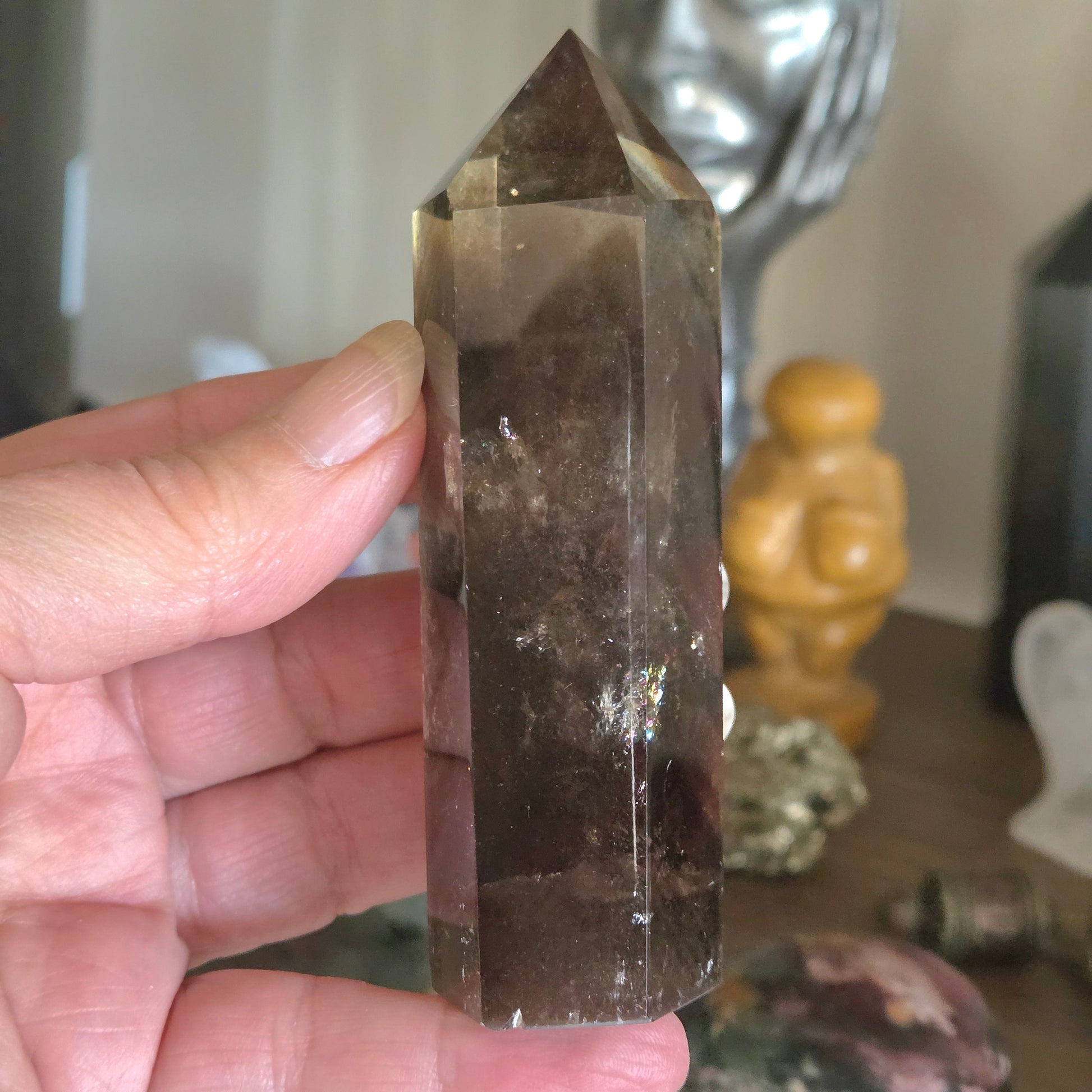 Person holding a crystal in front of a blurred background with decorative items.