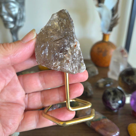 Hand holding a crystal on a gold stand with blurred crystals in the background