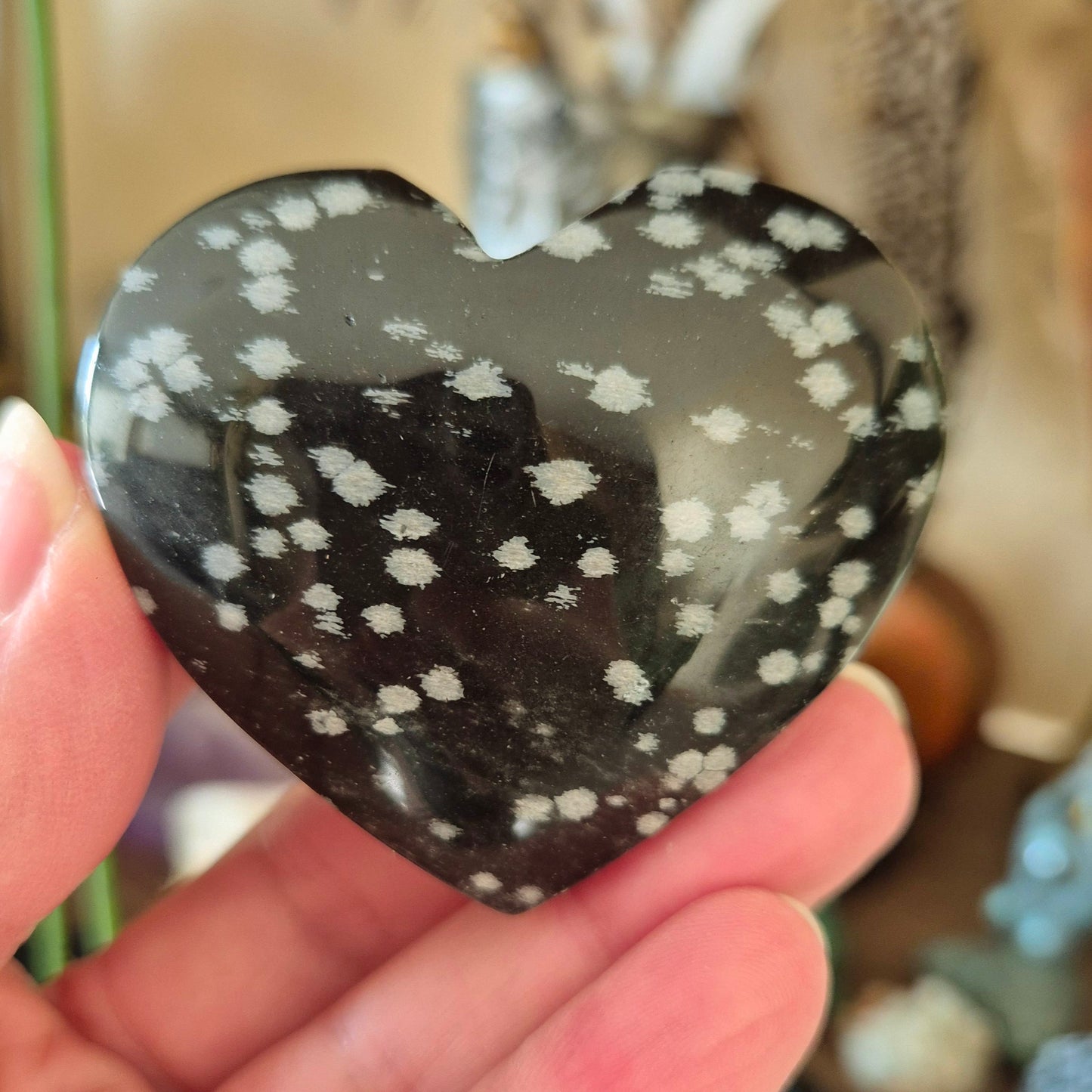 A hand holding a heart-shaped snowflake obsidian stone with a patterned surface.