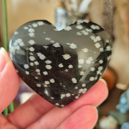 A hand holding a heart-shaped snowflake obsidian stone with a patterned surface.