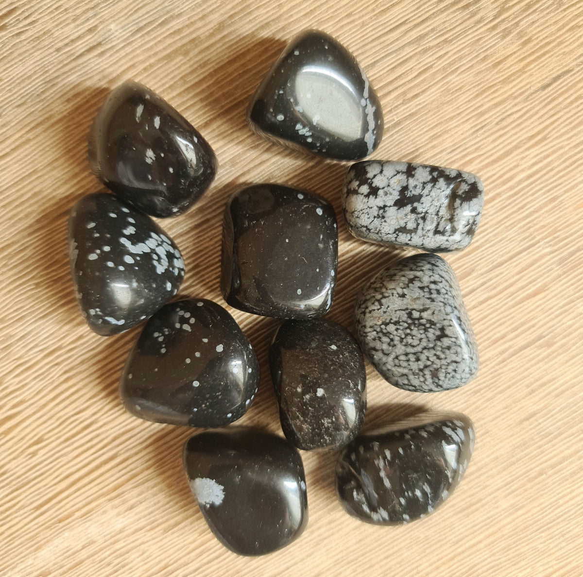 A collection of large Snowflake Obsidian stones with a smooth surface, displayed on a wooden surface.