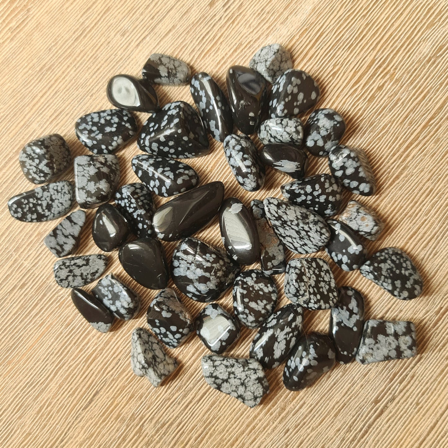 A collection of polished Snowflake Obsidian tumble stones with a black and white marbled pattern, displayed on a beige background.