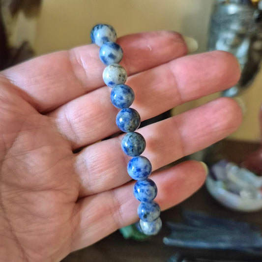 A sodalite bracelet held in a person's hand, featuring a series of smooth, blue sodalite beads with white calcite inclusions.