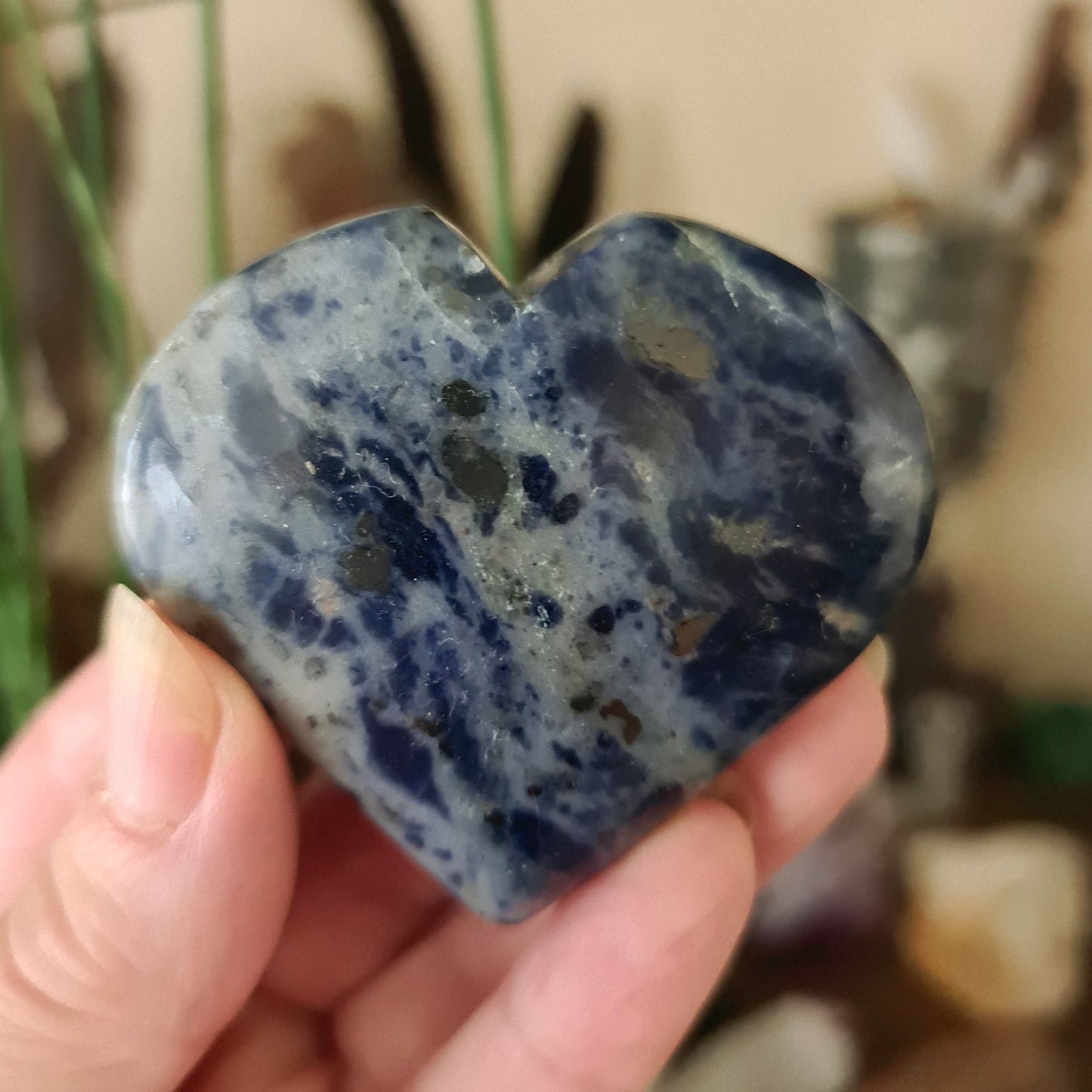 A sodalite heart-shaped stone held in a person's hand, with a bluish-gray color and natural pattern variations.