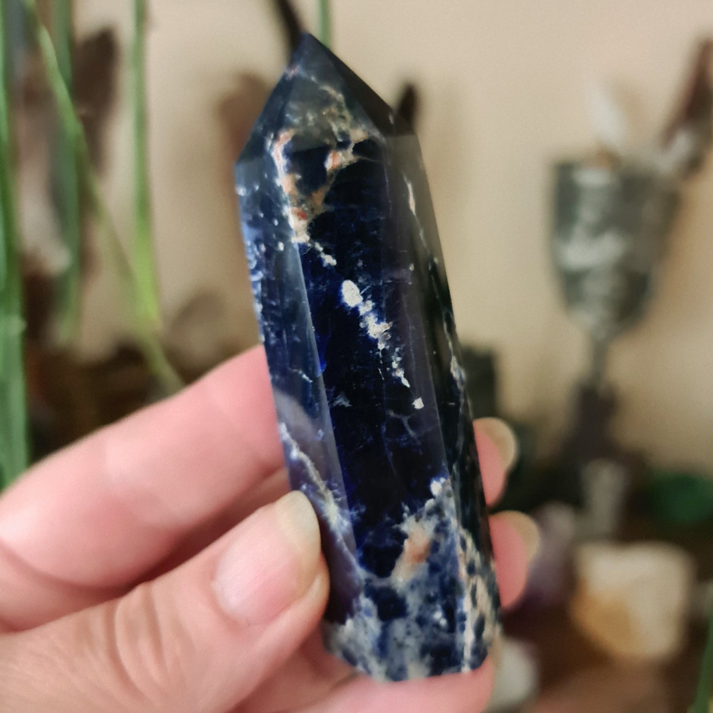 A sodalite crystal point being held in a person's hand, with a focus on its blue color and natural mineral patterns.