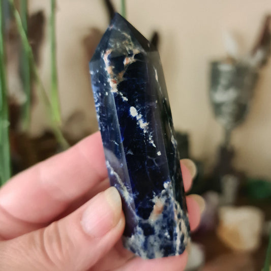 A sodalite crystal point being held in a person's hand, with a focus on its blue color and natural mineral patterns.
